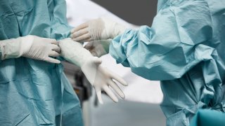 Midsection of female doctor helping surgeon wearing surgical glove.