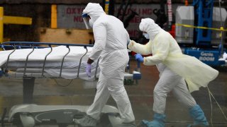 In this April 9, 2020 file photo, medical personnel move a deceased patient to a refrigerated truck serving as make shift morgues at Brooklyn Hospital Center in New York City.