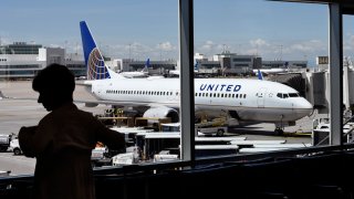 In this file photo, a passenger waiting for her flight to board stands in the airport terminal as a United Airlines plane is loaded at a gate at Denver International Airport in Denver, Colorado.