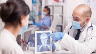 Médico con mascarilla contra el coronavirus que muestra el trauma cerebral del paciente en una tableta.