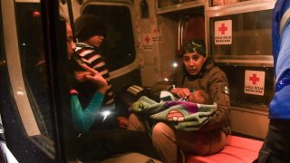 Fotografía de una socorrista de Cruz Roja que carga a un bebé de brazos, mientras un niño la observa