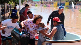 Varios hombres trasladan en lancha a una mujer y a un bebé en medio de una inundación